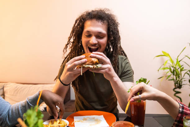 istock Young man with dreadlocks enjoying eating burger and drinking cocktail 1392191467