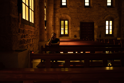 Young man is praying sitting on a bench inside of a church. Concept of religion.