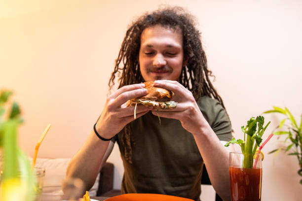 istock Young man with dreadlocks enjoying eating burger and drinking cocktail 1392191620