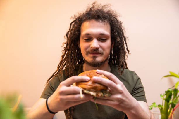 istock Young man with dreadlocks enjoying eating burger and drinking cocktail 1392191672