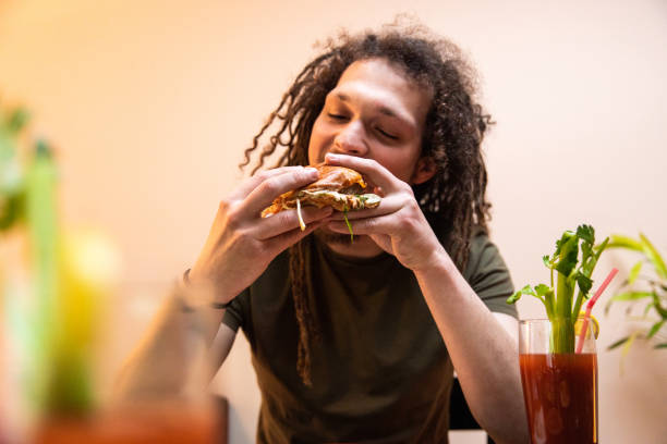 istock Young man with dreadlocks enjoying eating burger and drinking cocktail 1392191711
