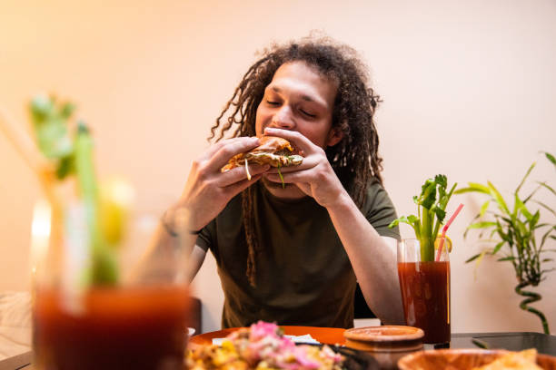 istock Young man with dreadlocks enjoying eating burger and drinking cocktail 1392192143