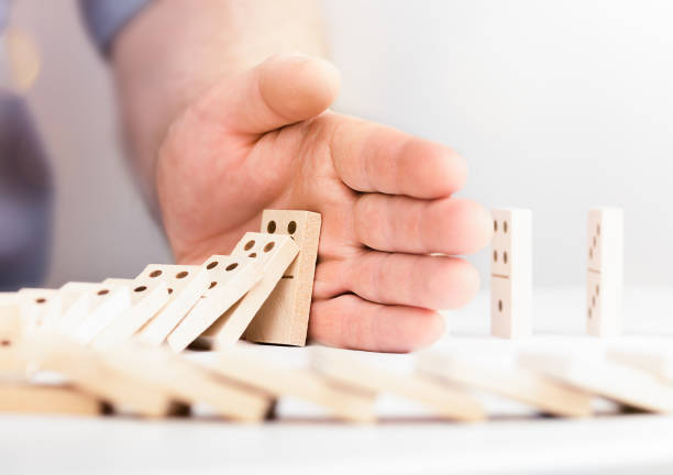 male hand stops falling dominoes, concept of risk and strategy in business