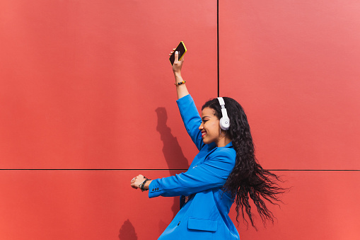 Girl dancing nonchalantly in the air in an urban scene. Woman on a red background, happy and crazy, dressed in retro 90s style blue clothes.