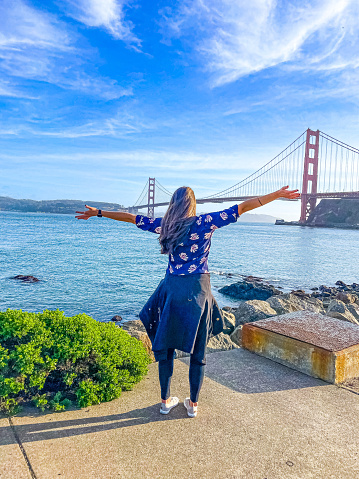 Woman facing Golden Gate Bridge with arms up in the arm
