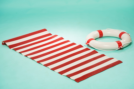 beach mat in red and white stripes and a life buoy on a turquoise pin-up background