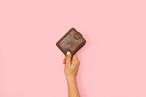 Woman hand holding a leather wallet on a pink background with copy space