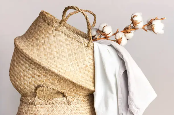 Straw wicker basket, natural cotton fabric, cotton flower branch on gray background. Bamboo basket stylish interior item eco design handmade. Decor of home. Natural eco materials, storage basket.