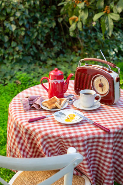 uma xícara branca com café, cafeteira vermelha, café da manhã e rádio estão em uma mesa em um jardim de verão. - coffee pot audio - fotografias e filmes do acervo
