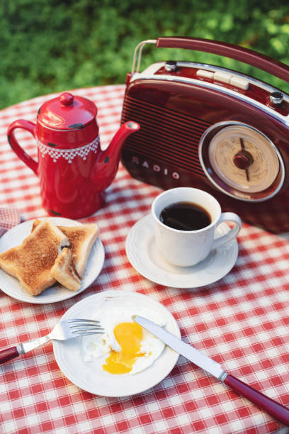 uma xícara branca com café, cafeteira vermelha, café da manhã e rádio estão em uma mesa em um jardim de verão. tema do café da manhã ao ar livre. - coffee pot audio - fotografias e filmes do acervo