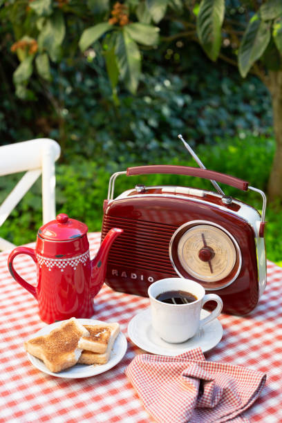 uma xícara branca com café, cafeteira vermelha e rádio estão em uma mesa em um jardim de verão. - coffee pot audio - fotografias e filmes do acervo