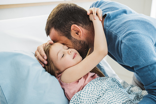 Little girl in hospital bed. Father is  with her and showing love and care.