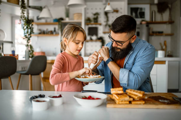 istock Handsome father and his little daughter decorating waffles, using icing bag 1392201584