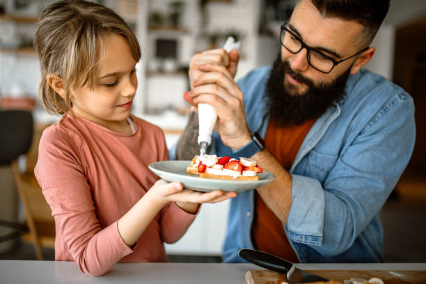 istock Handsome father and his little daughter decorating waffles, using icing bag 1392201636