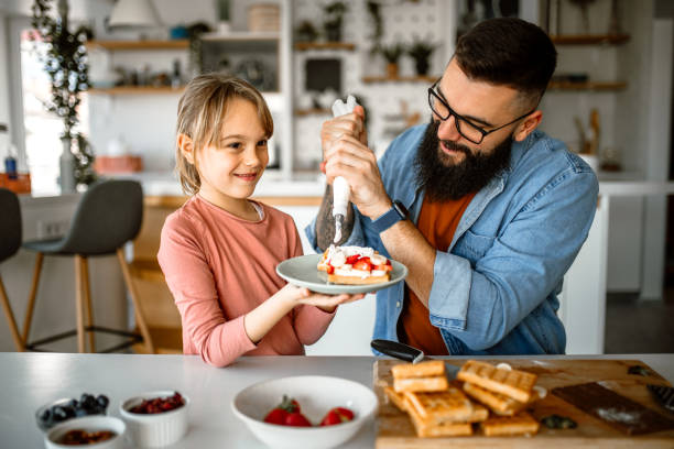 istock Handsome father and his little daughter decorating waffles, using icing bag 1392201682