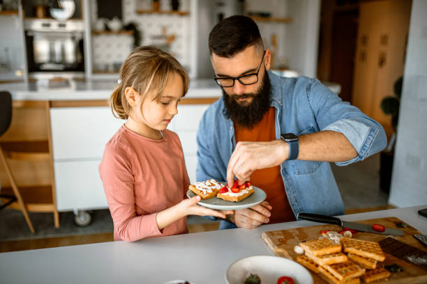 istock Cute little girl and her father preparing fruit for decorating waffles 1392201687
