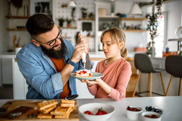 istock Handsome father and his little daughter decorating waffles, using icing bag 1392201688
