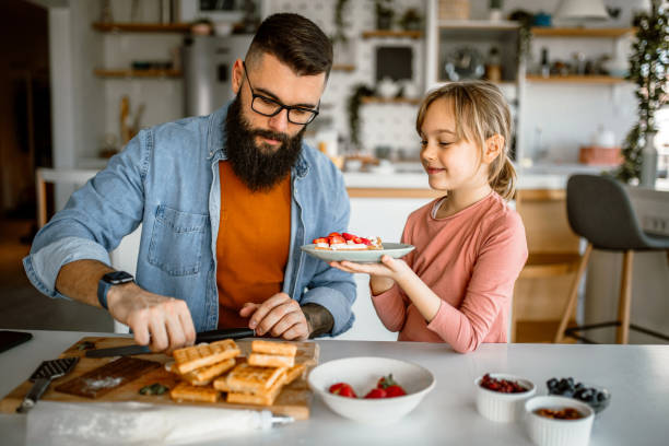 istock Daughter and father decorating waffles with strawberries, blueberries and bananas. 1392201721