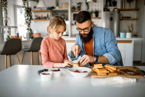 istock Daughter and father decorating waffles with strawberries, blueberries and bananas. 1392201768