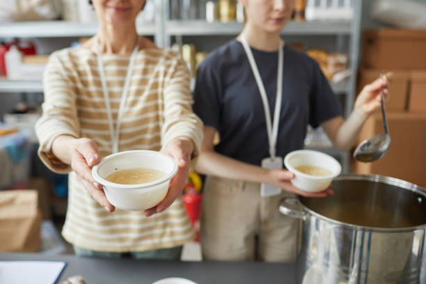 Sharing Food at Soup Kitchen Close up of two female volunteers giving out simple meals to people in need at soup kitchen of help center soup kitchen stock pictures, royalty-free photos & images