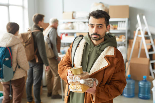 Man with Donations at Help Center Waist up portrait of young man holding food and water donations at volunteer center for refugees and people in need soup kitchen stock pictures, royalty-free photos & images