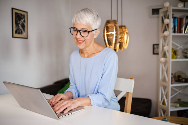 istock Cheerful senior woman smiling while using laptop at home 1392202796