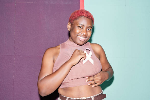 женщина использует розовую ленту на груди, чтобы поддержать причину рака молочной железы или спида. афроамериканка с короткими волосами. - breast cancer pink ribbon alertness стоковые фото и изображения