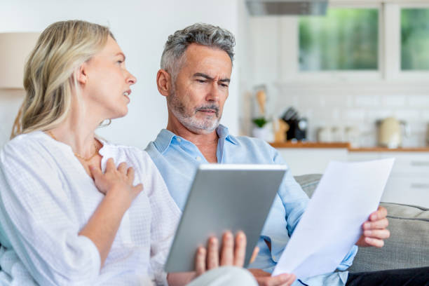 istock Worried mature couple using digital tablet and doing paperwork on the sofa. 1392204500