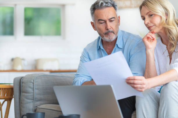 istock Happy mature couple using a laptop computer and doing paperwork on the sofa 1392204503