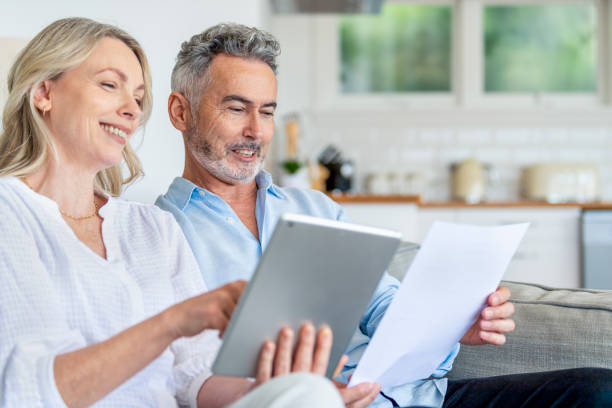 istock Happy mature couple using digital tablet and doing paperwork on the sofa. 1392204504