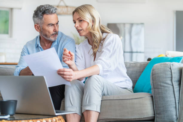 istock Mature couple using a laptop computer and doing paperwork on the sofa. 1392204507