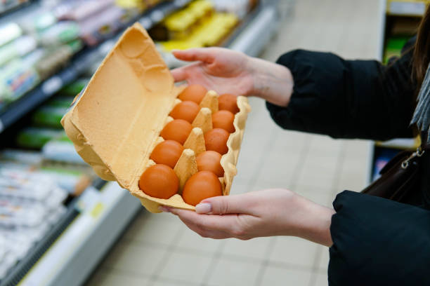 женщина выбирает куриные яйца в продуктовом магазине. заживать. - яйцо животного стоковые фото и изображения
