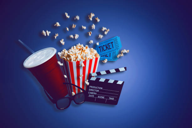 Conceptual photo of going to a movie theater Cinema theater concept. Composite of a box of popcorn, a large drink, a clapperboard, some 3D glasses and a couple of movie tickets on a dark blue background. box office stock pictures, royalty-free photos & images