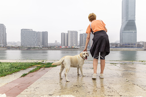 Mature woman standing with her Labrador dog by the river, after exercising outdoors.