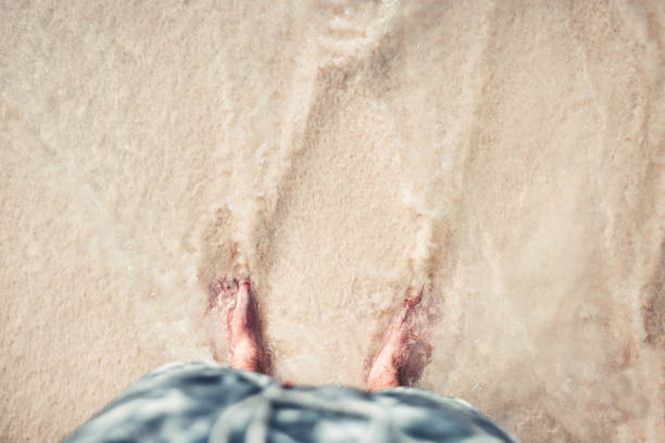 jeune homme debout sur la plage regardant vers le bas à pieds plage pov concept - swimming trunks shorts swimming shorts clothing photos et images de collection