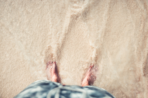 overhead photograph of some feet, on the shore of the beach, submerged in the water