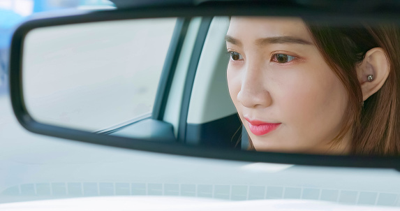 reflection of asian young businesswoman driving happily in the car from rearview mirror while commuting