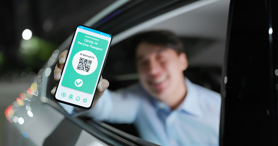 asian man shows health passport on mobile phone which indicates a vaccination against covid-19 while commuting in taxi at night