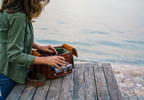 Female photographer with a retro camera and leather bag near the beach