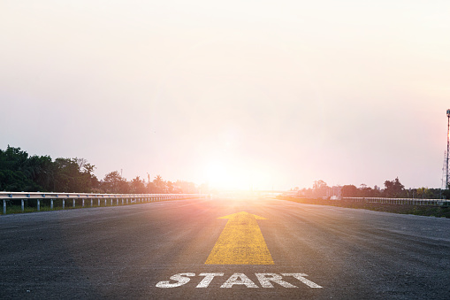 Start line wording with yellow arrow to glowing sunlight on super high way for business and challenge plan of career path concept.