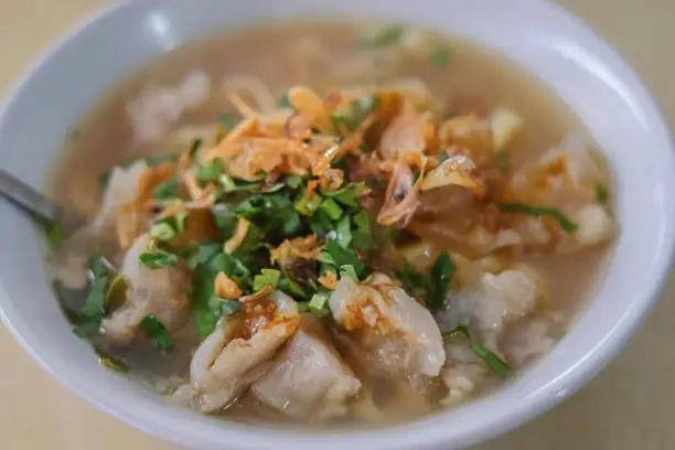 Close-up shot of a bowl of mie kocok kikil Bandung, a traditional Indonesian beef noodle soup from Bandung, West Java. The dish consists of noodles served in rich beef broth with "kikil," which are slices of cow's trotters.