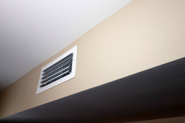 An unrecognizable person holding the remote control in front of the air conditioner at home