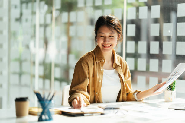istock Smiling young Asian office worker at startup business while working on a laptop computer Inside a modern office. 1392243160