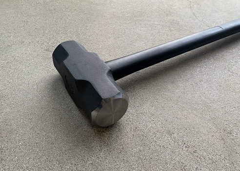 Closeup of a sledgehammer on a concrete floor.