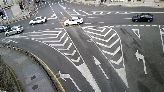 Road markers on an crossroads, traffic islands,  cars passing by. Lugo city, Galicia, Spain.