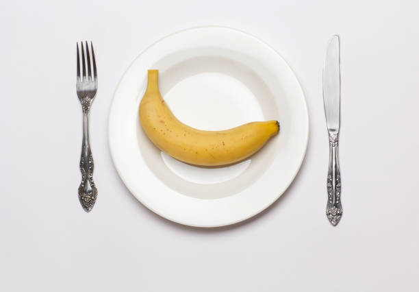 istock One banana on white plate with fork and knife on white background 1392256585