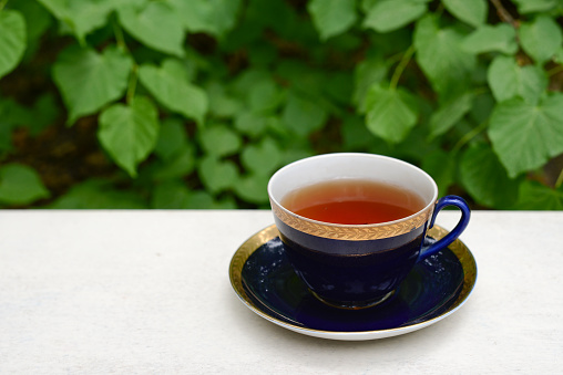 tea cup, black tea, herbal tea, blue cup, tea couple, tea ceremony, tea party, tea china, outdoor tea, cobalt blue, gold border on the cup, gold border cup, summer, spring, leisure, table, veranda, breakfast, coffee, coffee cup, blue tea cup on the back porch, blurred background with tree view green forest, countryside, cozy atmosphere suitable for relaxing on vacation
