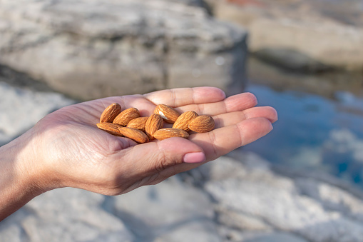 A handful of almonds in a woman's hand against the background of nature. Blurred background