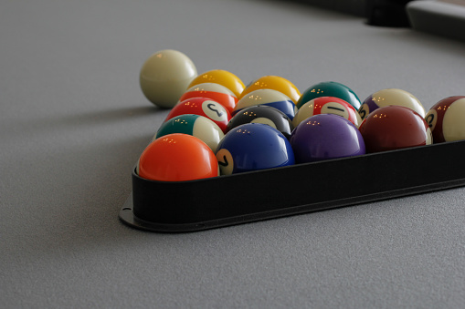 A view of a set of pool balls organized inside a triangle rack on a grey felt pool table.