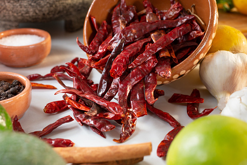A closeup view of a spilled bowl of dried chile de arbol, among other salsa ingredients.